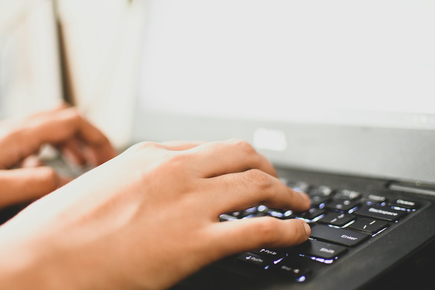 Hände tippen auf einer leuchtenden Laptop-Tastatur bei Nacht.